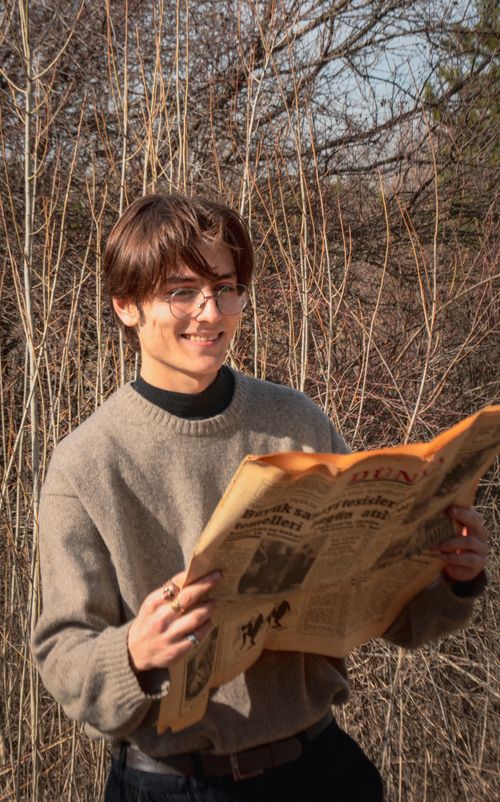 Free Smiling young man with glasses reads a vintage newspaper outdoors in a rural setting. Stock Photo