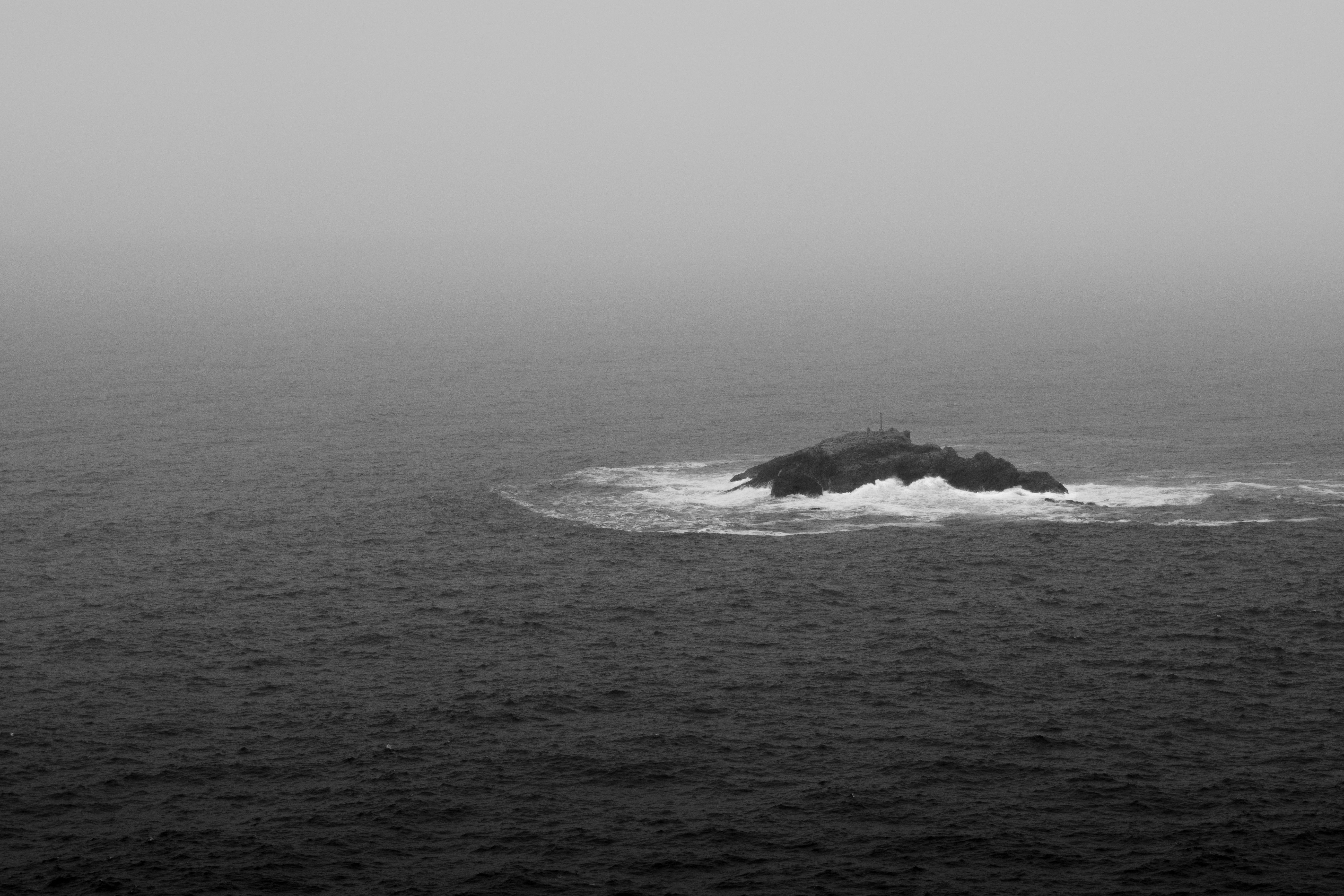 Black and white aerial view of a misty island in Rio de Janeiro, surrounded by ocean waves.