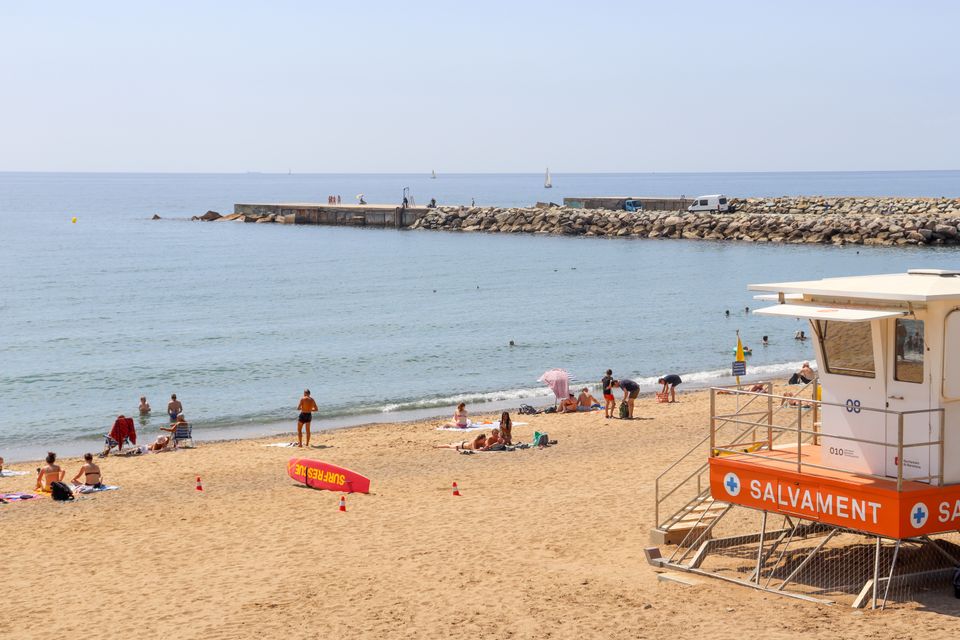 Lively beach scene at Barceloneta in Barcelona, featuring a lifeguard tower and sunbathers.