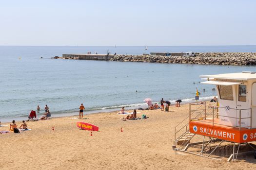 Lively beach scene at Barceloneta in Barcelona, featuring a lifeguard tower and sunbathers.