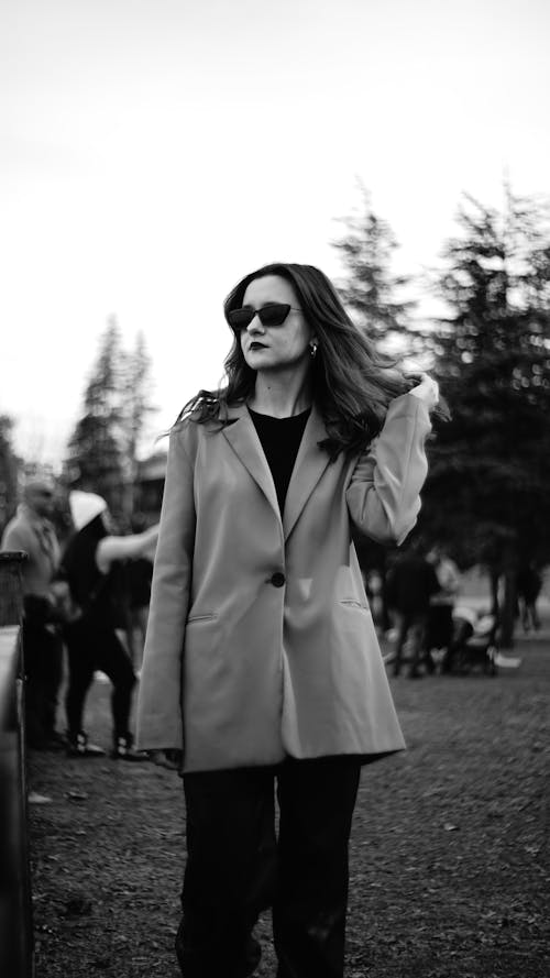 A woman in a coat and sunglasses standing in a park