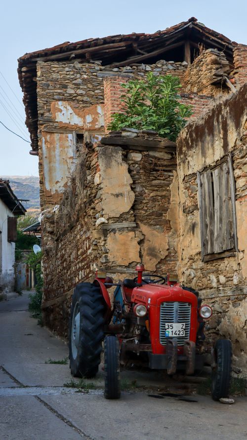 Free Abandoned vintage tractor parked on an old town street by weathered stone walls. Stock Photo