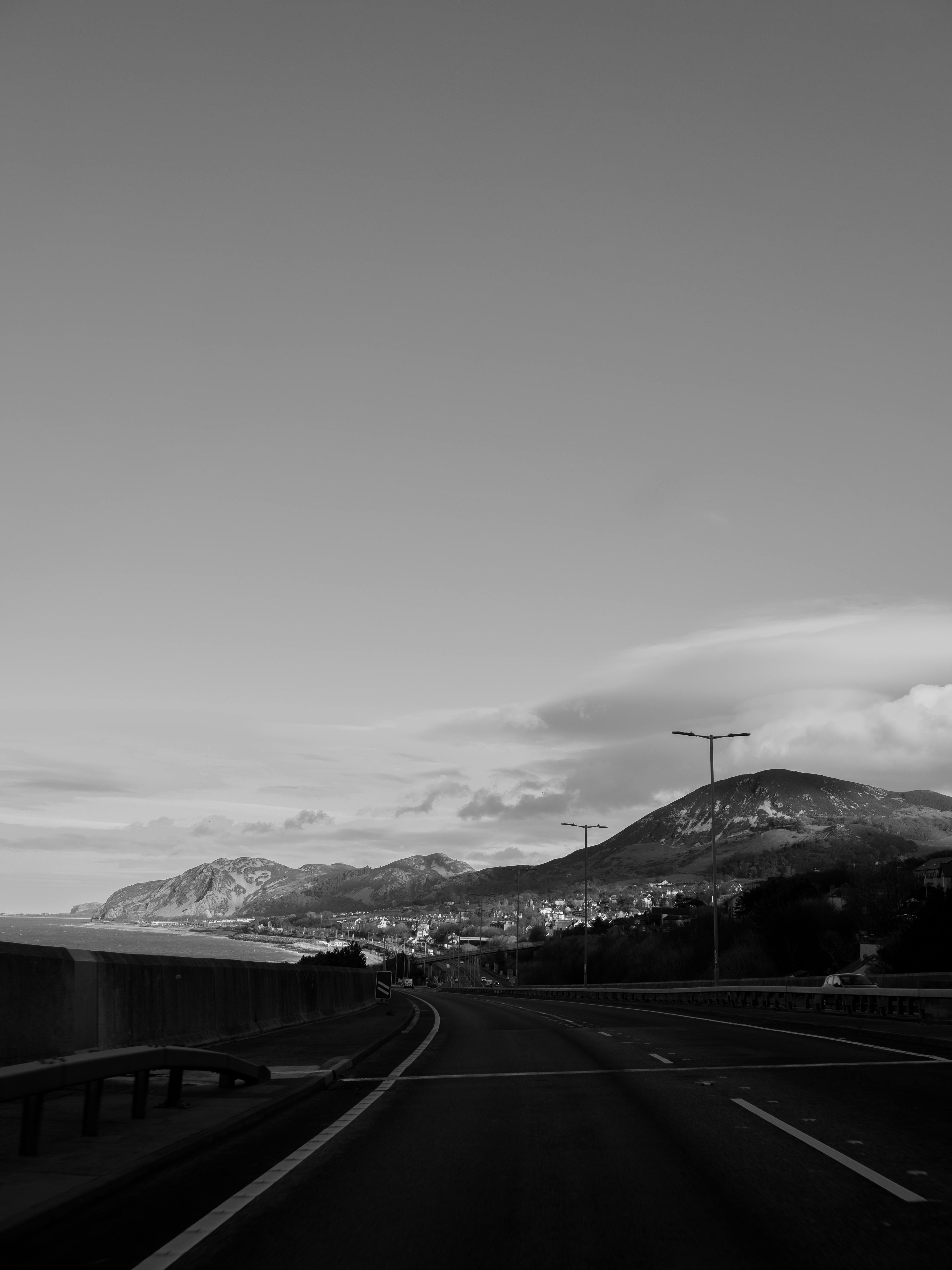 Black and white photo of a scenic road by hills in Conwy, Wales on a calm day.