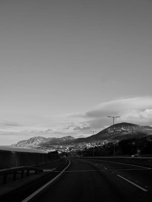 Black and white photo of a highway with mountains in the background