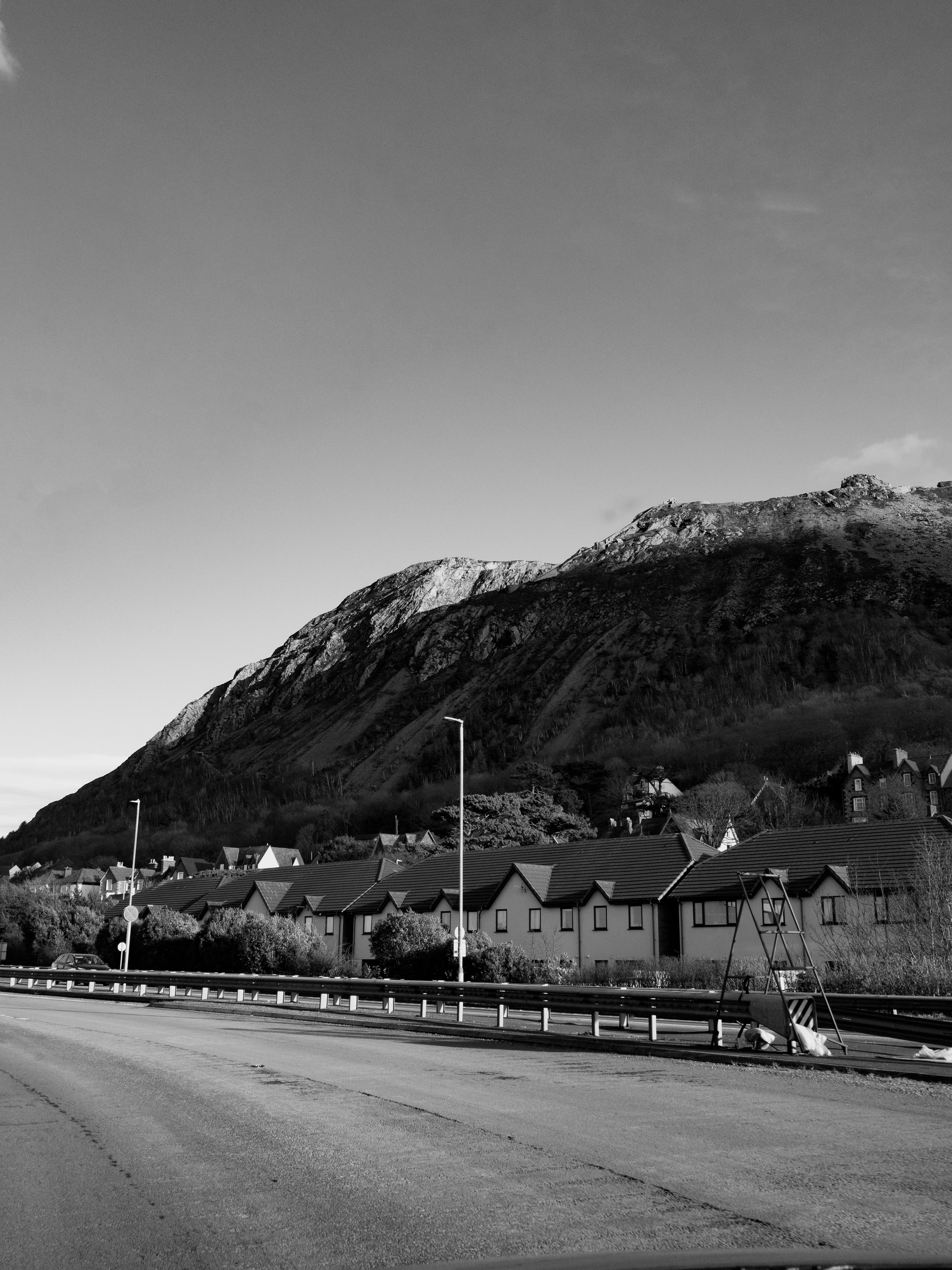 Black and white capture of Penmaenmawr, Wales, featuring rugged mountain and residential area.