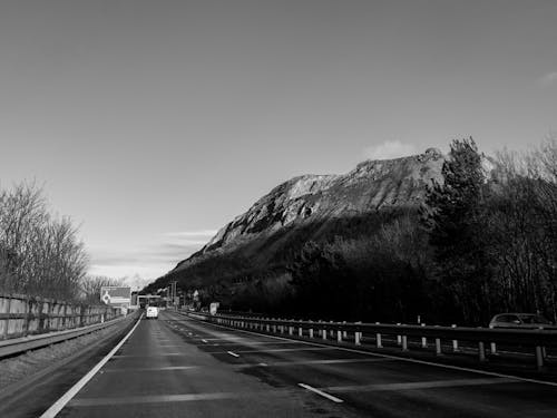 A black and white photo of a highway with mountains in the background
