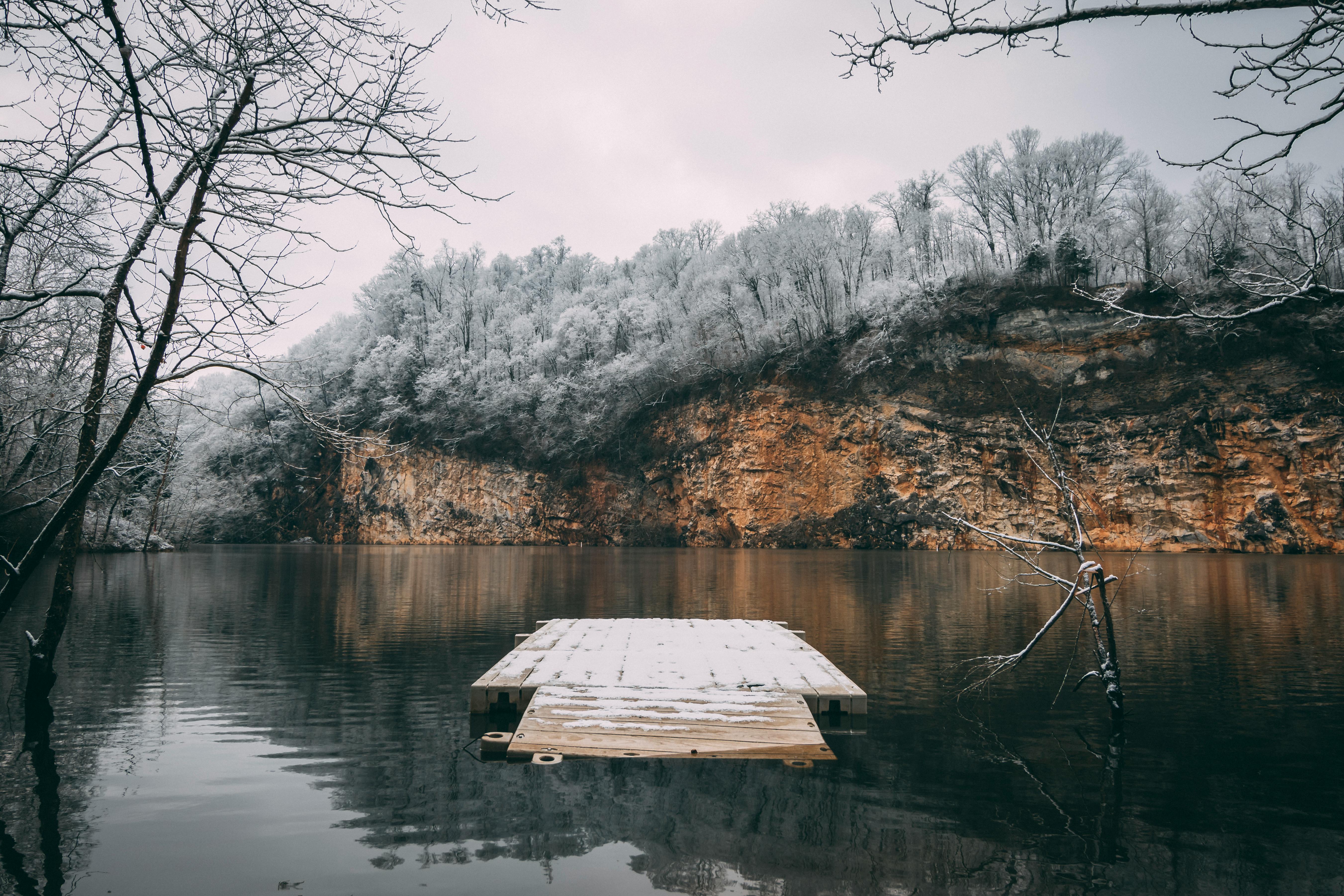 冬日景象宁静，白雪覆盖的码头通向宁静的湖泊，四周悬崖环绕，树木也披着银装