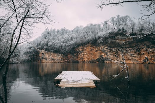 冬日景象宁静，白雪覆盖的码头通向宁静的湖泊，四周悬崖环绕，树木也披着银装