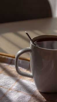A tranquil morning scene with a tea mug and spoon in soft sunlight on a checkered cloth.