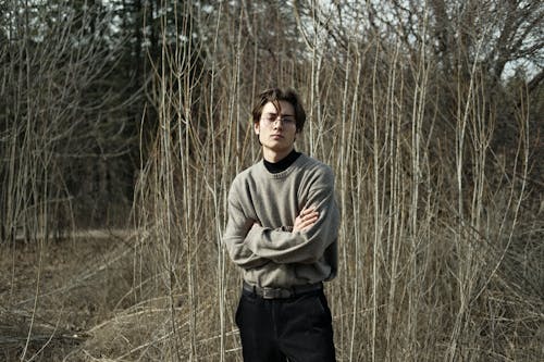 Model in a Gray Sweater and Black Pants Standing Among Leafless Shrubs