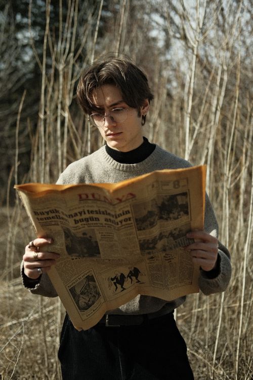 Free A man with eyeglasses reads a newspaper in a rustic outdoor setting during autumn. Stock Photo