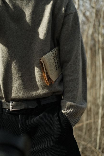 Man in sweater holding vintage newspaper outdoors in natural light setting.