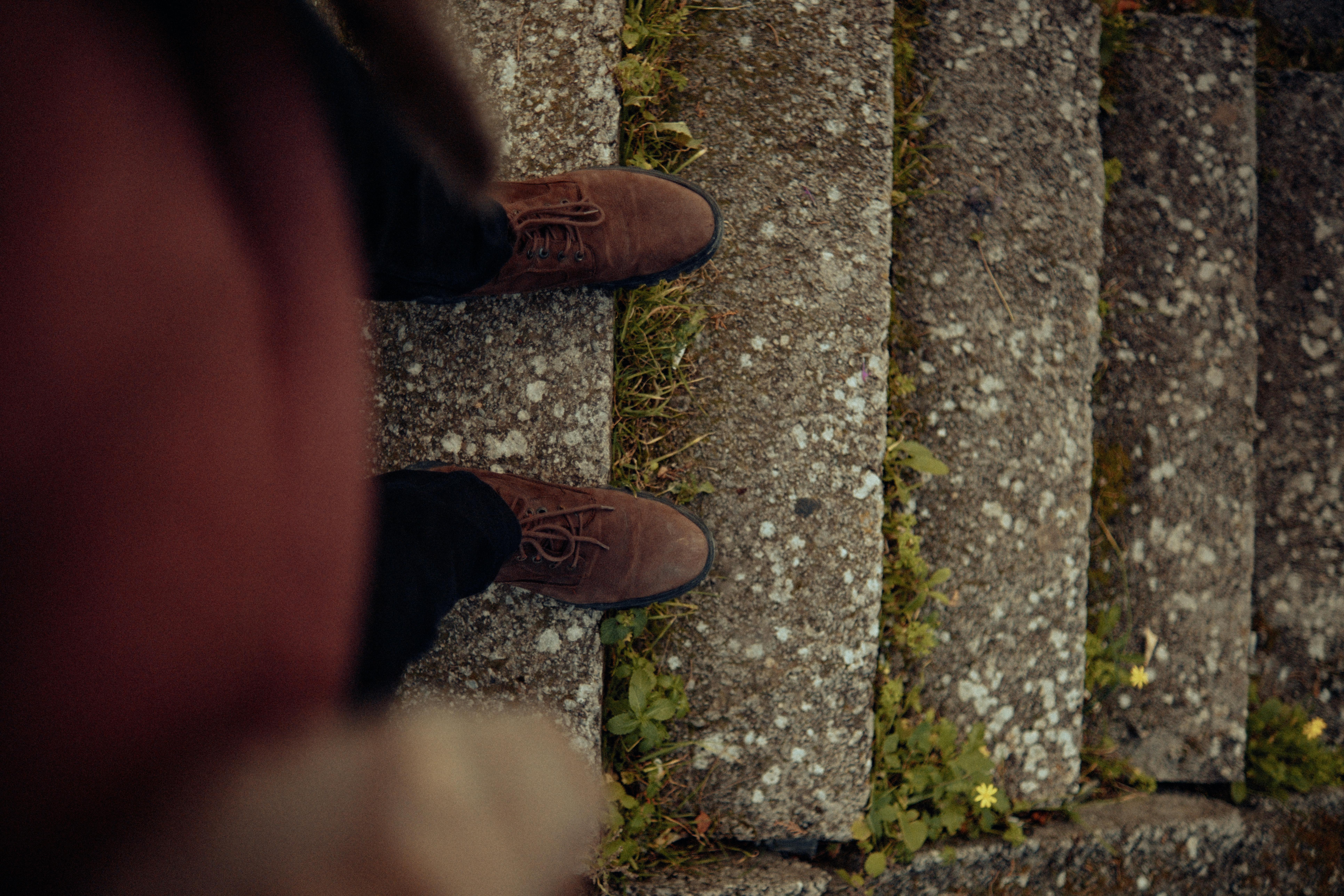 Brown shoes on mossy stone steps, viewed from above with surrounding greenery.
