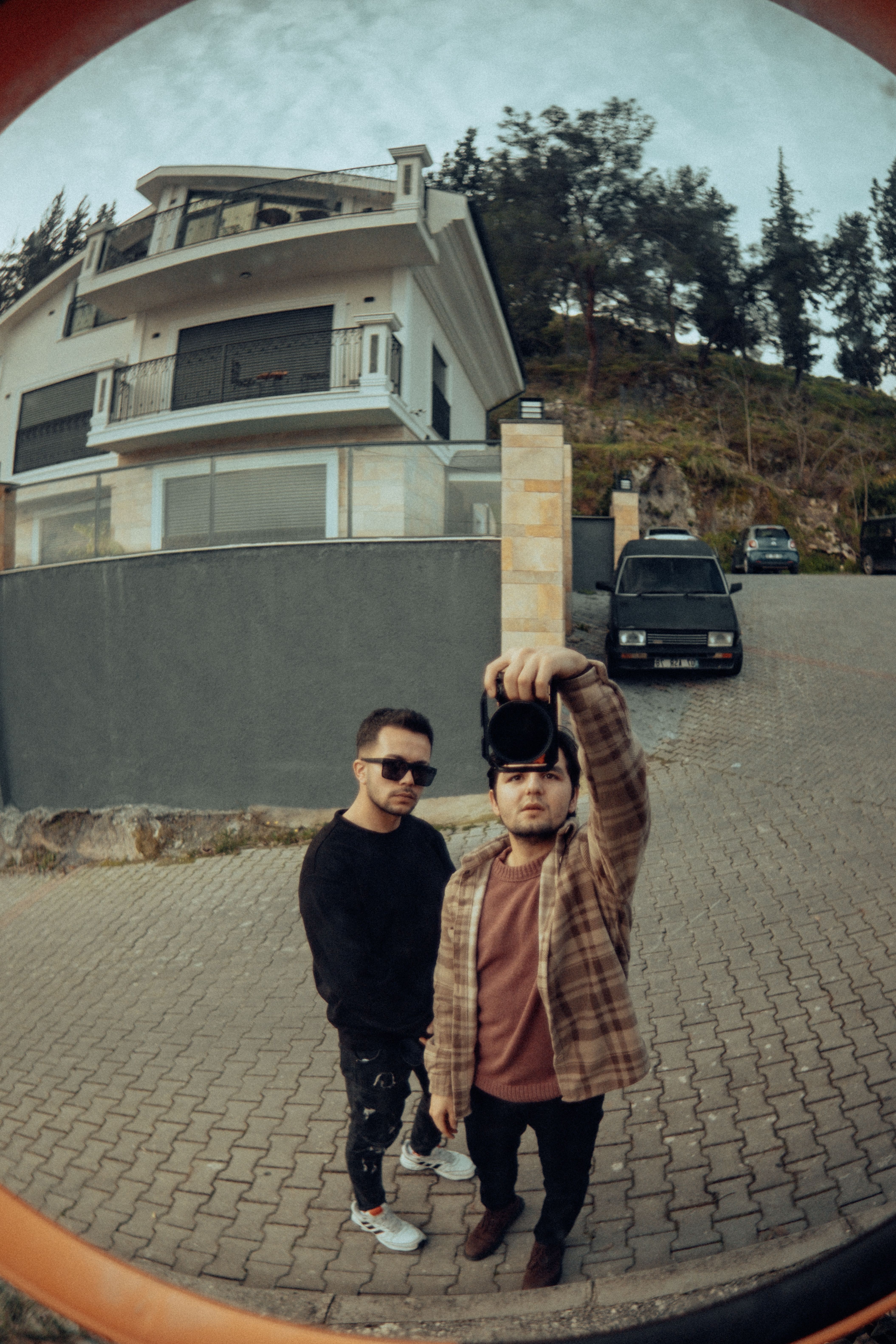 Two men taking a selfie using a fisheye lens reflecting a street view.
