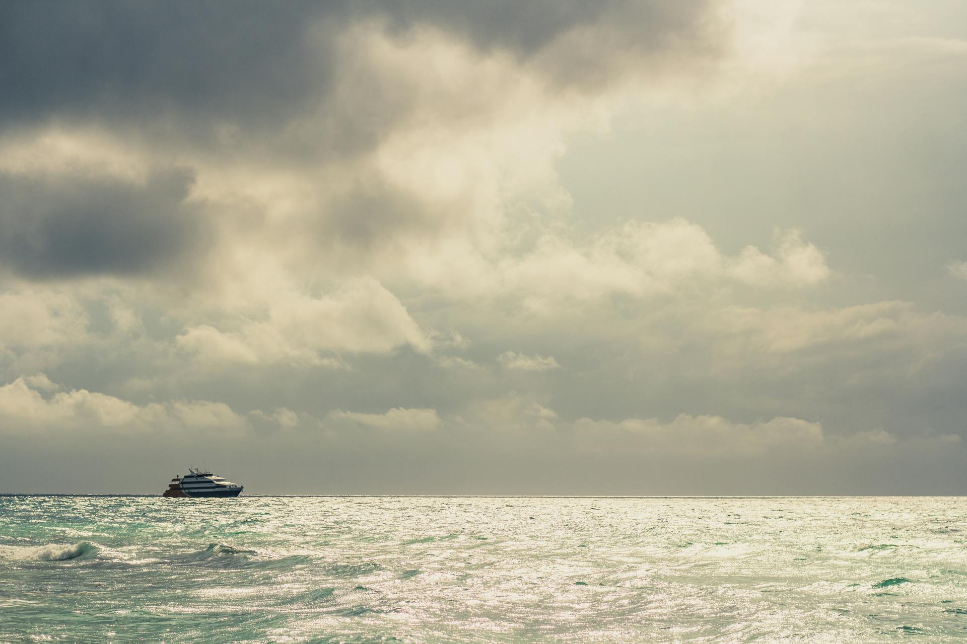 A tranquil ocean scene at Playa del Carmen with a distant cruise ship under cloudy skies.