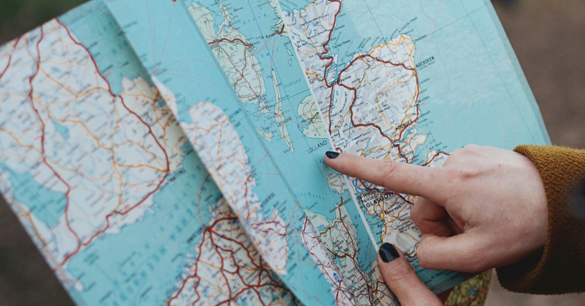 A woman holds a map while navigating through an outdoor park trail, pointing at a location.