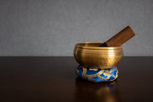 A golden colored Tibetan singing bowl with striker inside standing on a ring cushion isolated on a blurred clean background and empty space for text. Spirituality and meditation concept