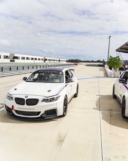 Free Two white sports cars parked on a race track under a cloudy sky, ready for a race. Stock Photo