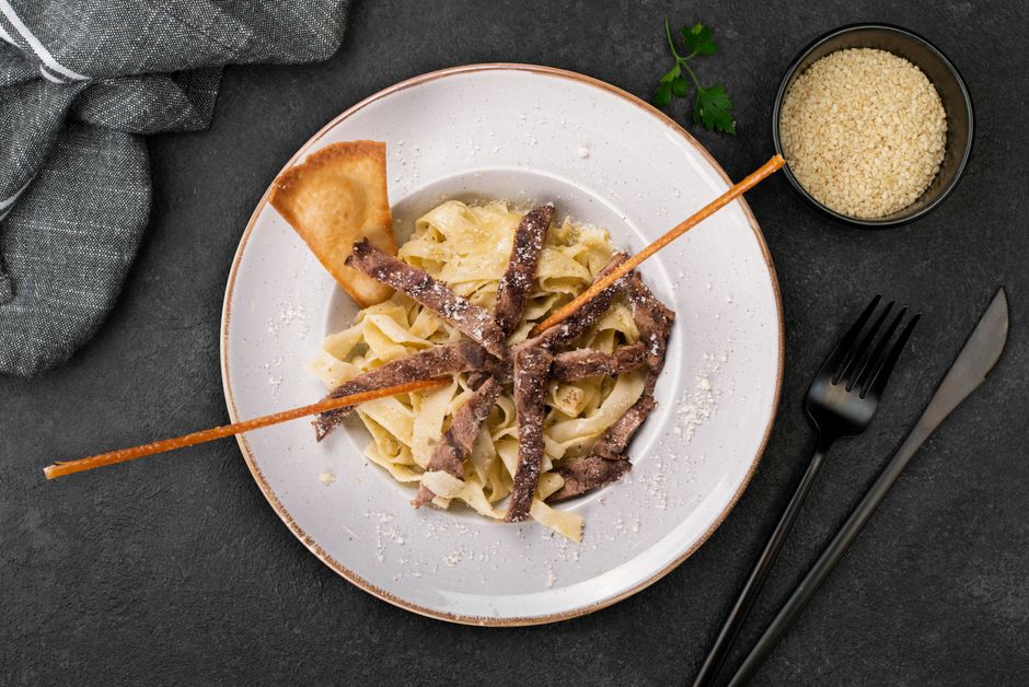 Thin slices of seared steak fanned over a bowl of pasta tossed in garlic butter sauce, topped with shaved parmesan and cracked pepper