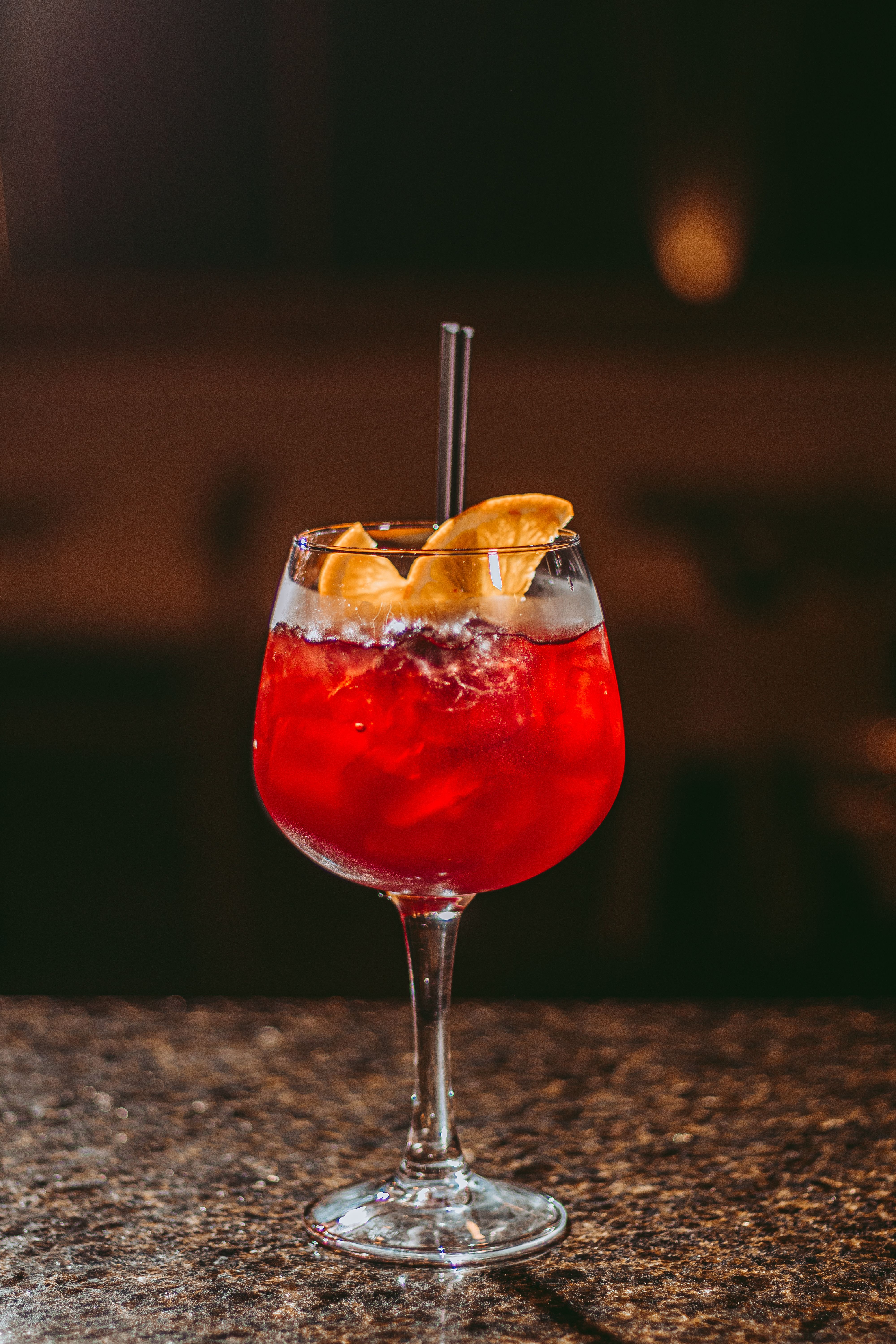 A tall glass of pink-orange Bay Breeze cocktail filled with ice, garnished with a lime wedge and pineapple wedge, condensation beading on the glass.