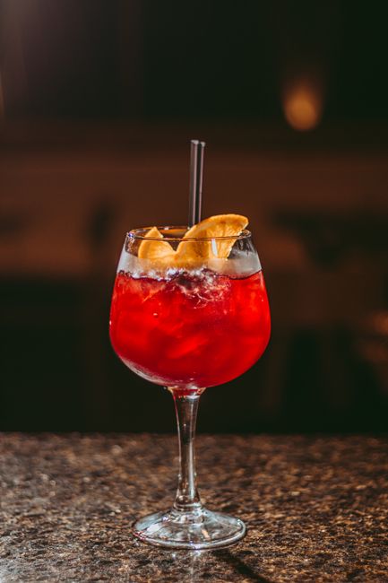 A tall glass of pink-orange Bay Breeze cocktail filled with ice, garnished with a lime wedge and pineapple wedge, condensation beading on the glass.