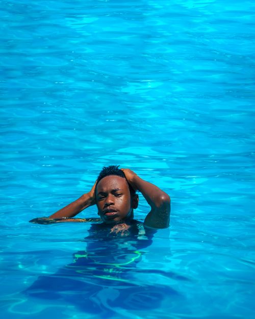 Free A man enjoying a leisurely swim in a bright blue swimming pool during summer, promoting relaxation and recreation. Stock Photo