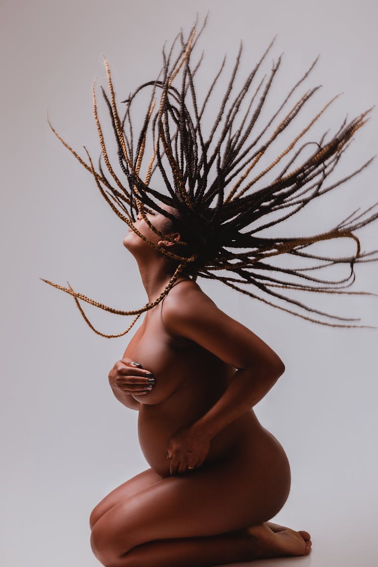 Naked, Pregnant Woman Kneeling And Shaking Dreadlocks