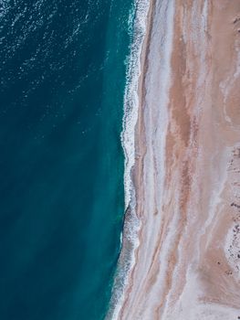 A stunning aerial view of a turquoise beach with foamy waves in Antalya, Türkiye, showcasing natural beauty.