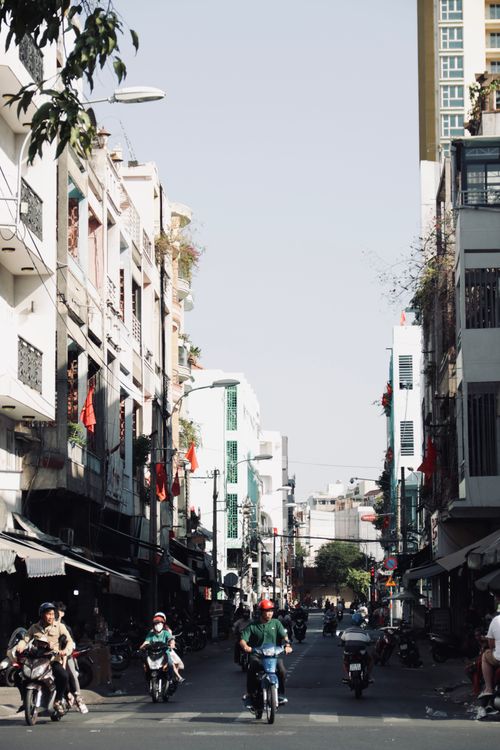 Free A vibrant city street in Vietnam with people riding motorbikes under a clear sky. Stock Photo