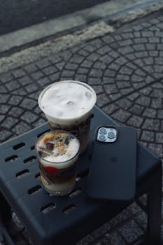 Overhead view of iced coffees and smartphone on outdoor chair, urban setting.