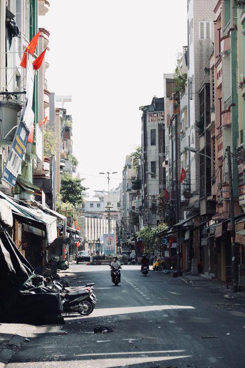 Free A vibrant city street in Vietnam featuring motorbikes and tall buildings under a bright summer day. Stock Photo