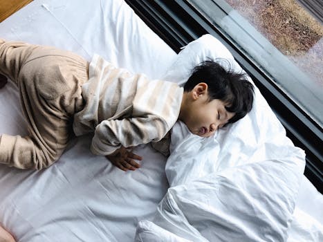 An Asian child peacefully sleeping in cozy pajamas by a window, indoors.