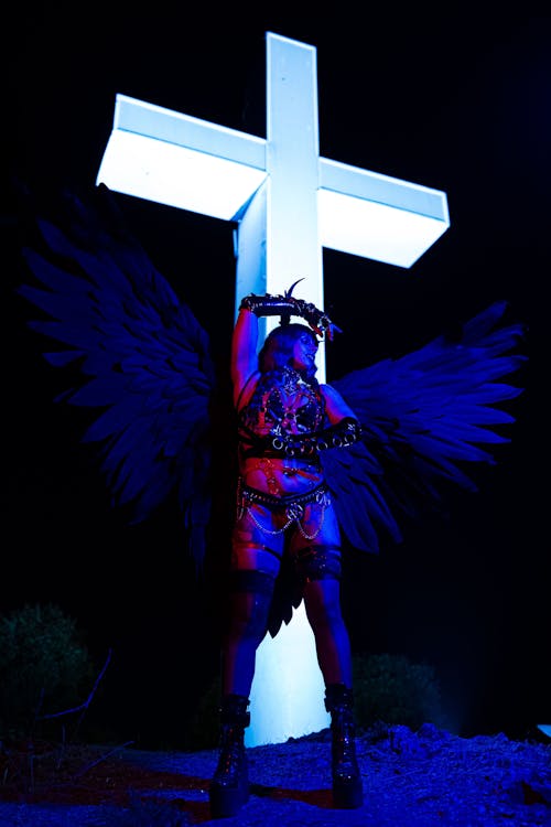 Angel in Lingerie Stands by Illuminated Cross