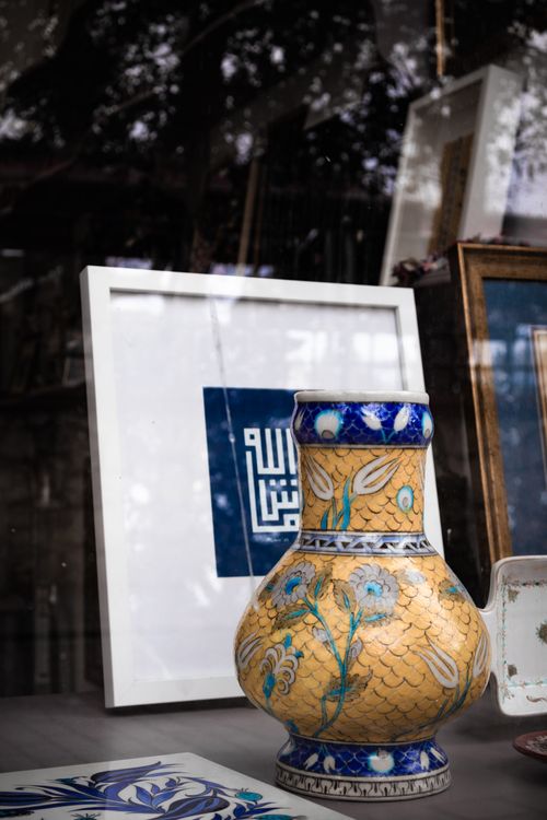 Free Artistic ceramic vase with floral patterns displayed with decorative frames in a window. Stock Photo
