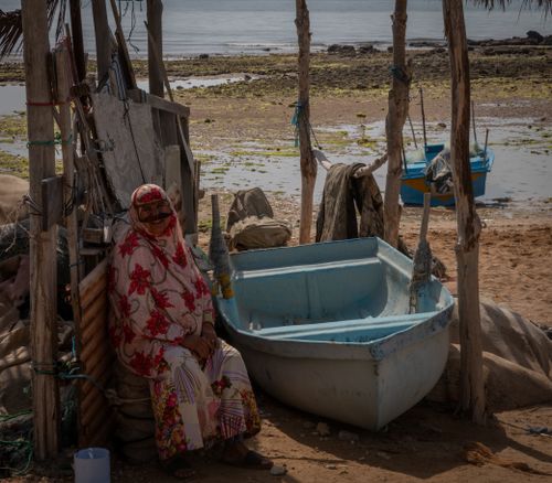 Free A woman sitting near a makeshift shelter and boat on a rugged coastline. Stock Photo