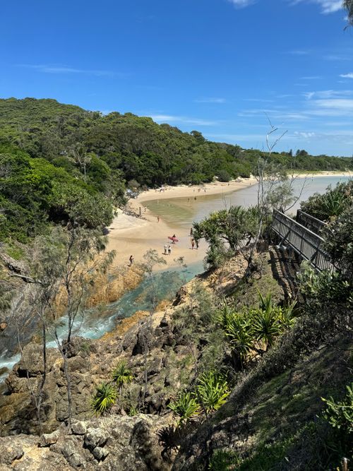 Free A serene beach cove with lush greenery and rocky cliffs on a sunny day. Stock Photo