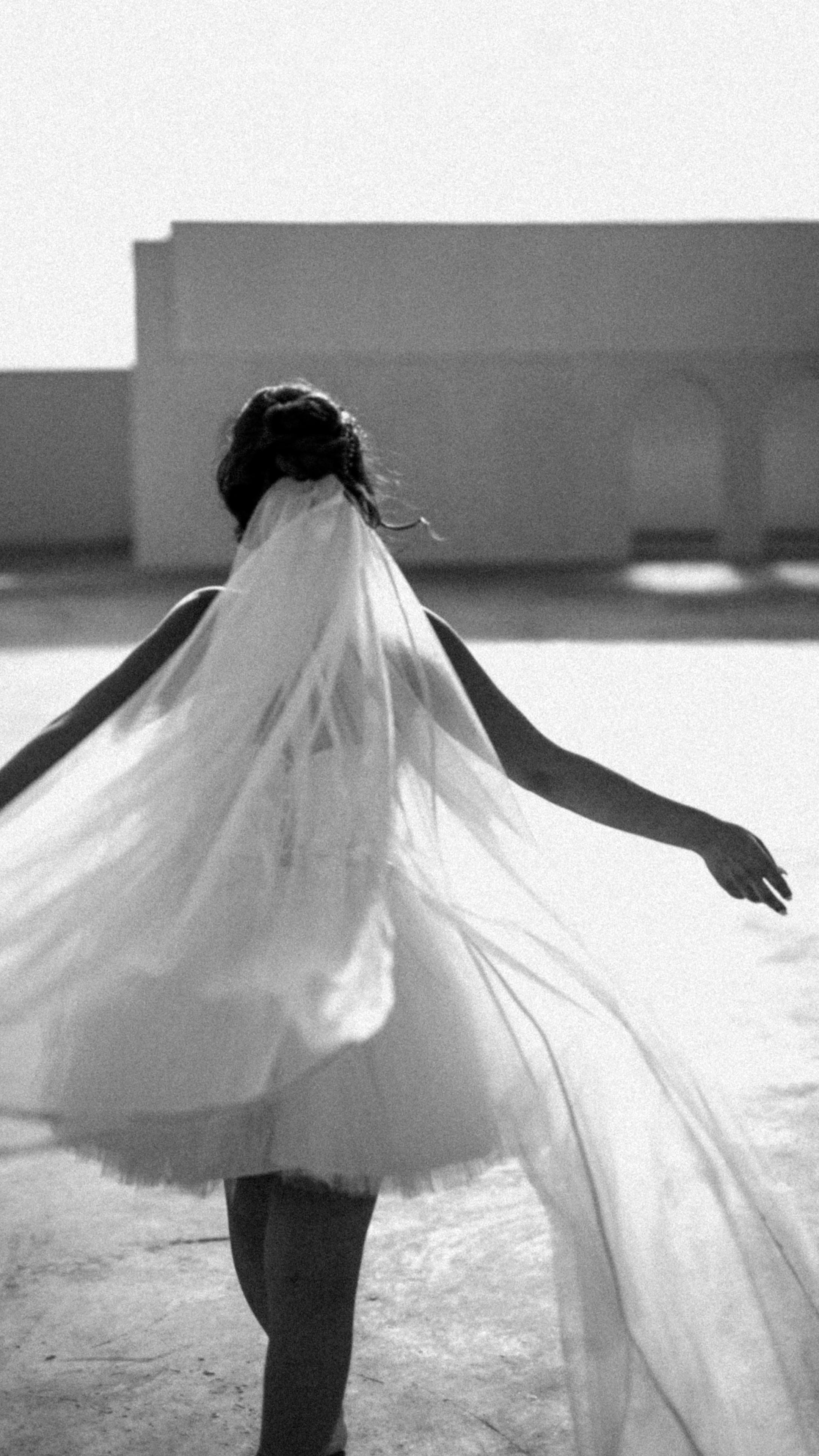 Elegant back view of a bride in motion with a flowing veil, captured in black and white.