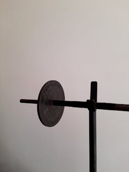 Close-up of a rustic barbell with a gray iron weight against a neutral background.
