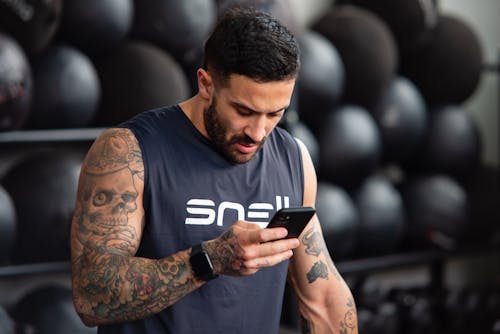 A Muscular, Tattooed Man Using His Phone at the Gym 