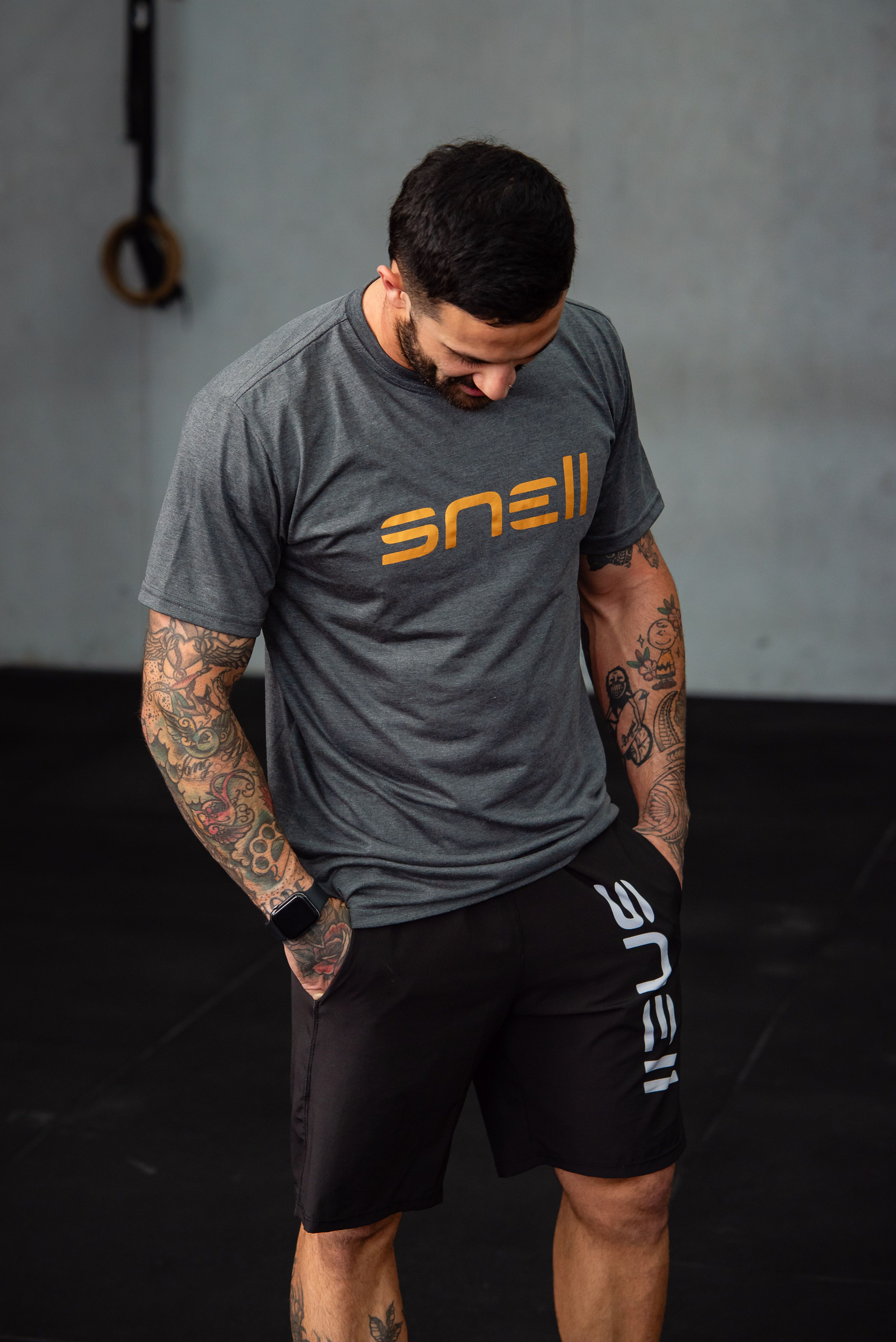 Man with tattoos standing in a gym, wearing a branded sports outfit.