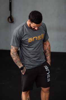Man with tattoos standing in a gym, wearing a branded sports outfit.