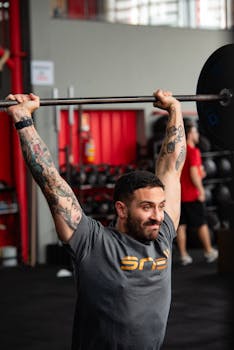 Tattooed man lifting weights in a gym showcasing strength and focus.