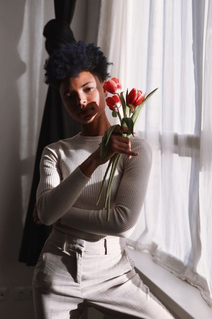 Stylish young woman holding tulips, captured in soft window light in Berlin.