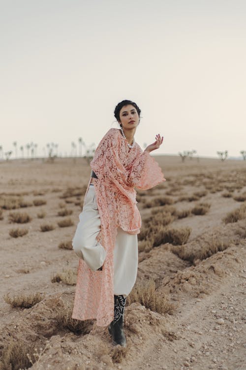 A woman in a pink robe and white pants standing in the desert