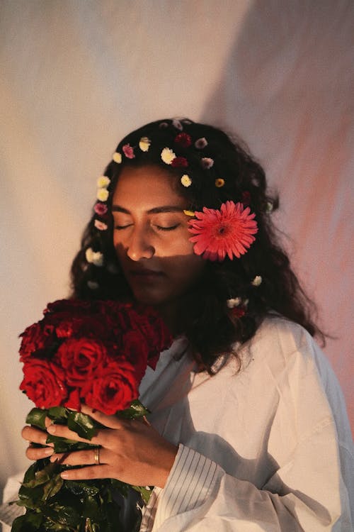 Young Woman with Flowers Braided in Her Hair Enjoying the Scent of a Bouquet of Roses