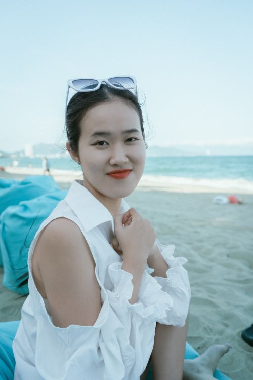 Free Portrait of a woman in a white blouse enjoying a day at the beach with ocean in background. Stock Photo