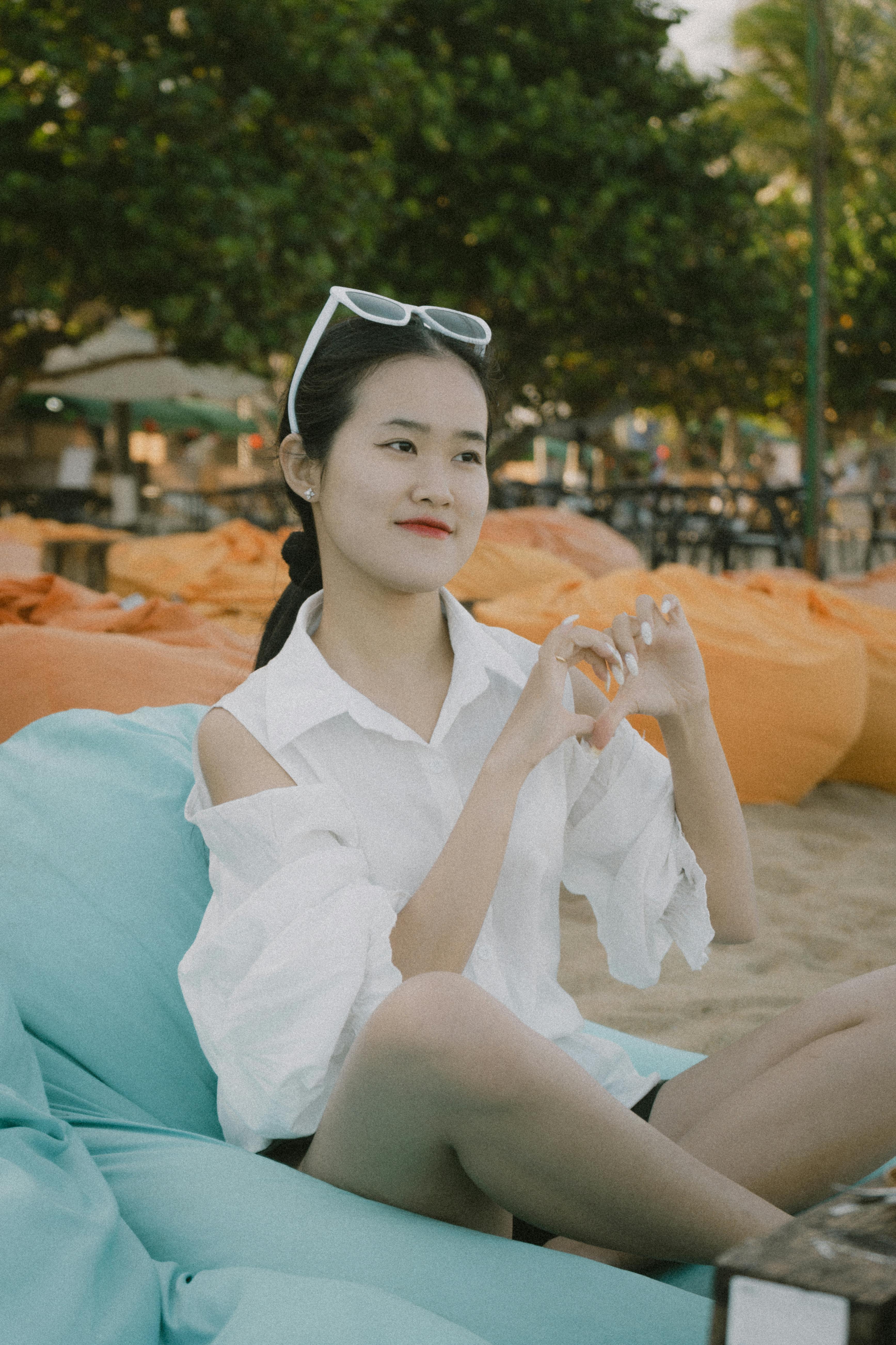 Free A young woman enjoys a summer beach setting, seated on a bean bag with a playful hand gesture. Stock Photo