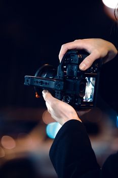 Close-up of hands holding a camera with a cage for stability during nighttime photography.
