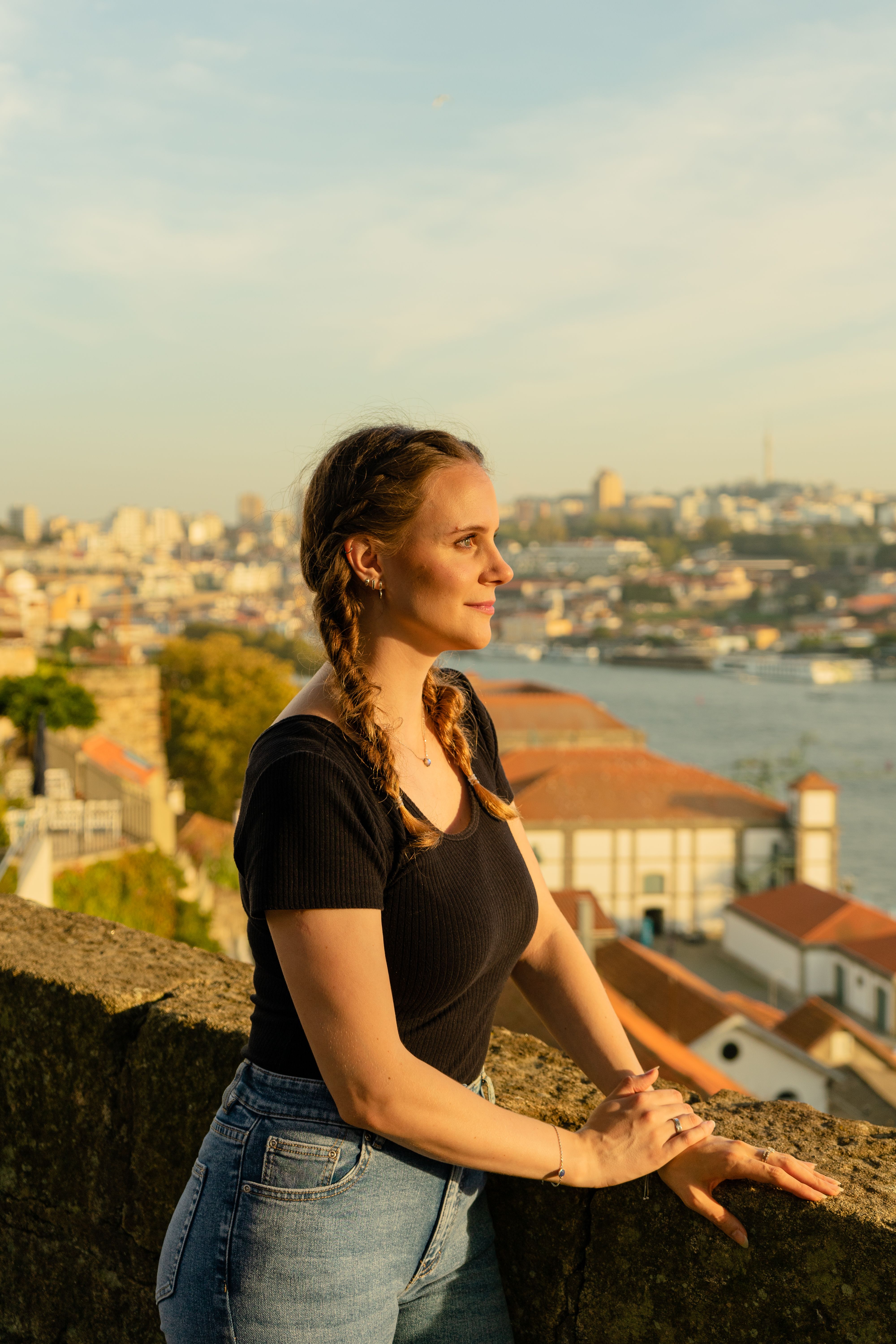 A woman in casual attire admires the beautiful Porto skyline at sunset.