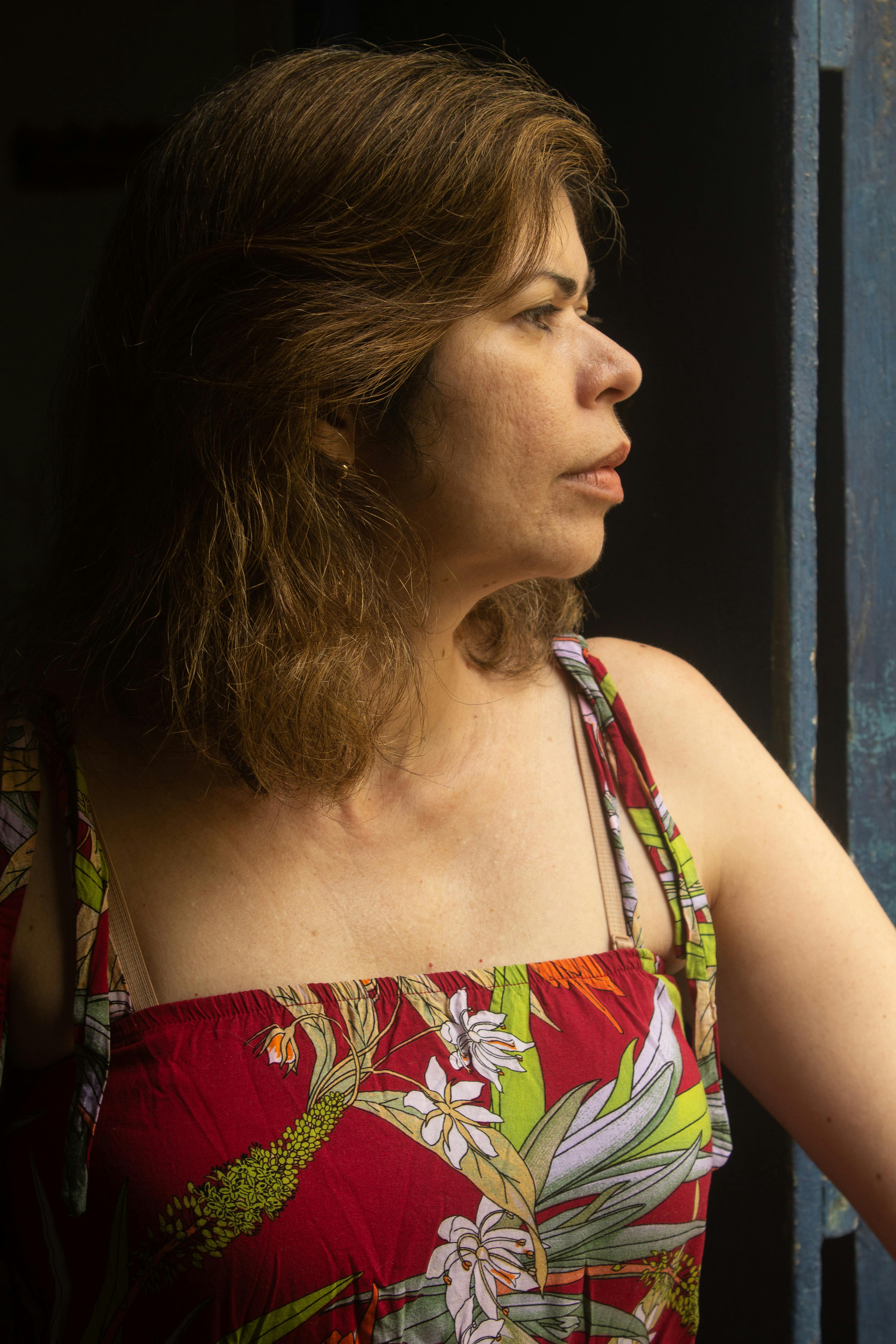 Side view portrait of a woman in a floral dress gazing thoughtfully out a window.